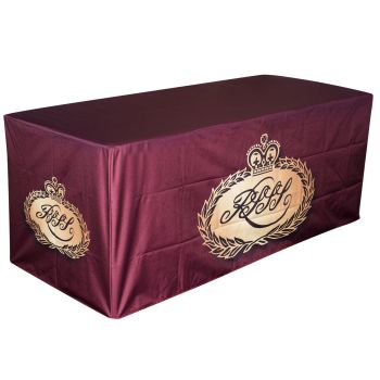 An angled view of a 4ft fitted table cover for tradeshows in Canada. The cloth is burgundy coloured and has a golden crown logo on the front for branding.